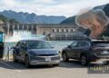 Two cars are parked near a hydroelectric dam and EV charging station, illustrating electric vehicles vs gas cars. One car charges with a blue glow; the other is surrounded by smoke and an orange explosion. Mountains and water form the backdrop: “The Sanity Project.”.