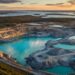 A large open-pit mine with terraced sides and turquoise water collects at the bottom, highlighting Canada’s critical minerals. Smaller pools dot the landscape, surrounded by forest and lakes under a golden sunset. The Sanity Project logo appears in the lower right corner.