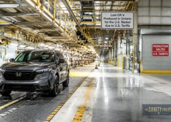 A gray Honda CR-V sits on a factory floor under bright lights. Signs mark it as the last U.S.-bound model made in Ontario due to tariffs, highlighting the broader industry shifts in lithium battery comparison, like LFP vs NMC battery choices.