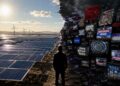 A person stands at the divide between a sunny field of solar panels and wind turbines on the left, and a dark, chaotic wall of glitching TV screens and protest signs spreading renewable energy misinformation on the right.